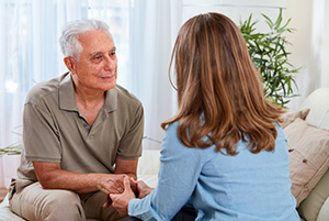 Las vegas home health care speech therapy woman with brunette hair with her back towards us wearing a blue shirt speaking with an elderly caucasian male.