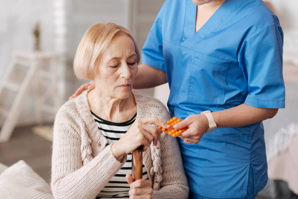 A nurse assists an elderly woman by holding out a pill