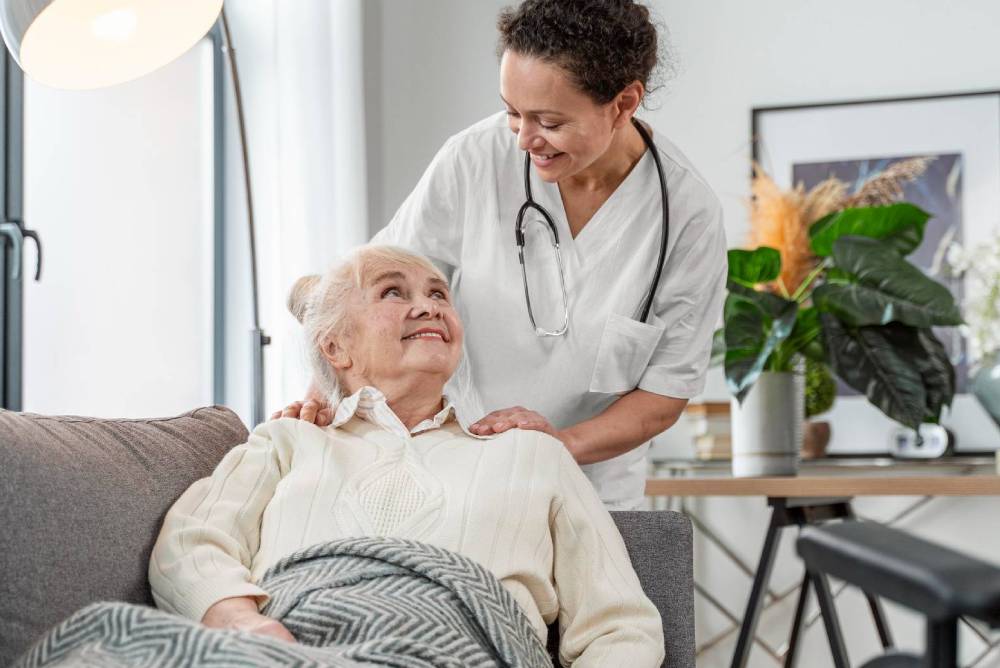 A nurse comforts a elderly woman reclined on a couch