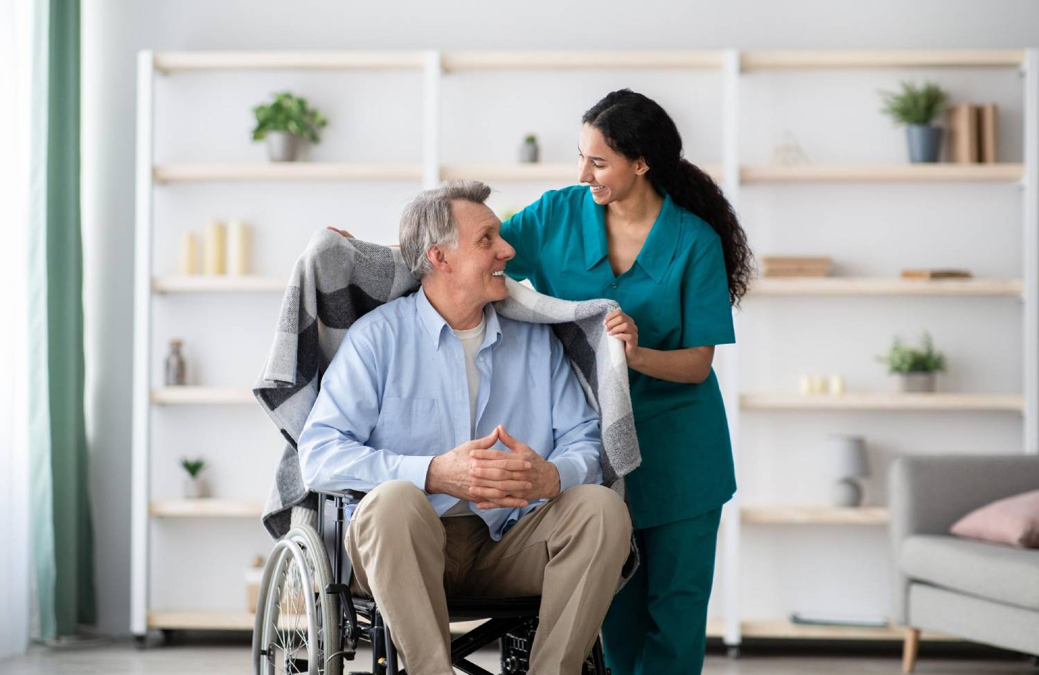 Adult man in a wheelchair with a nurse in green scrubs standing next to him