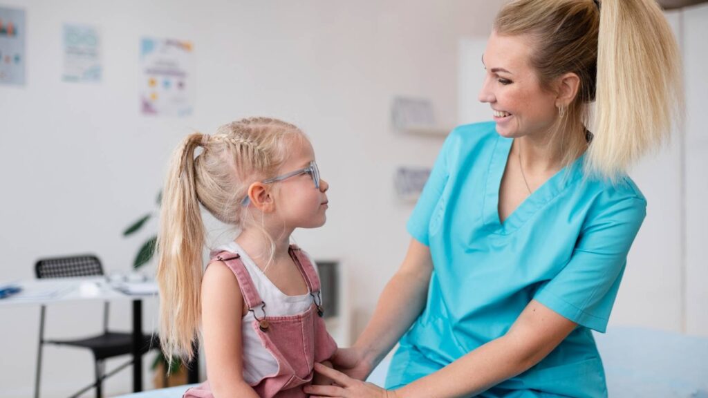 Nurse in scrubs and little girl with glasses smiling