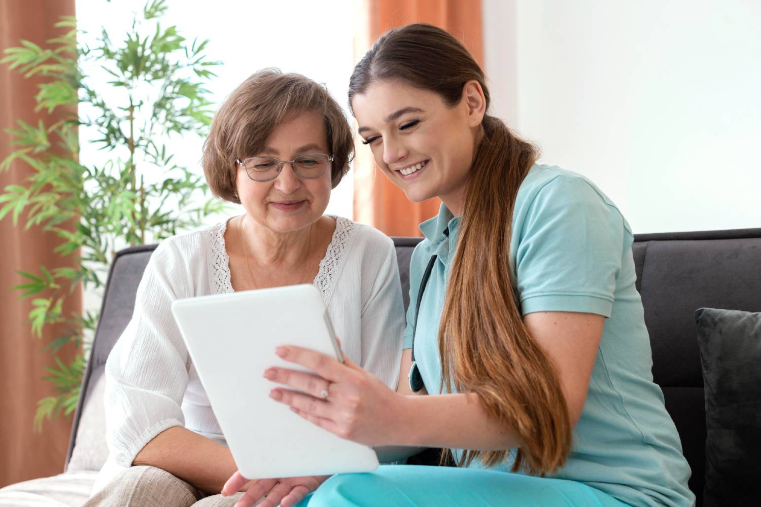 Young nurse reading from a tablet with a older woman sited next to her