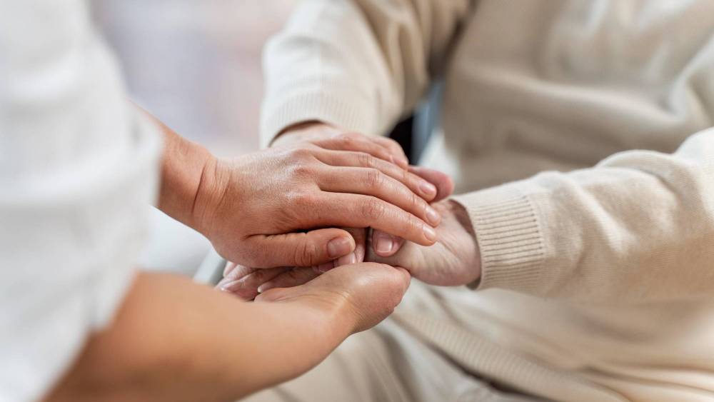 A compassionate nurse gently holds the hand of an elderly patient